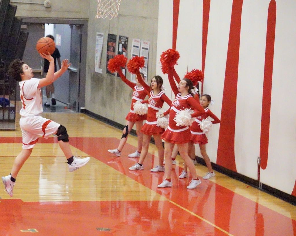 kid jumping and shooting with cheerleaders in background