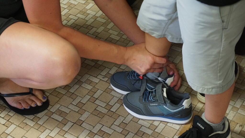 An adult helping a child try on a pair of shoes