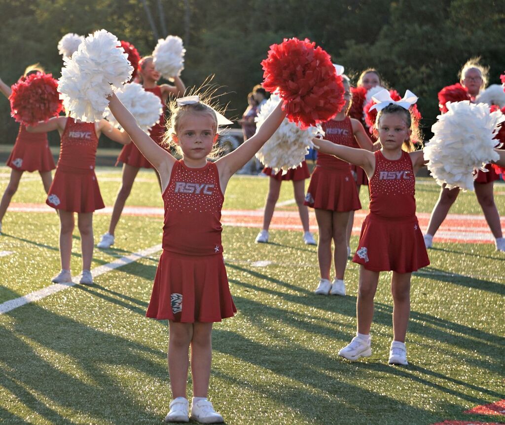 A youth cheerleader with pom poms in the air 