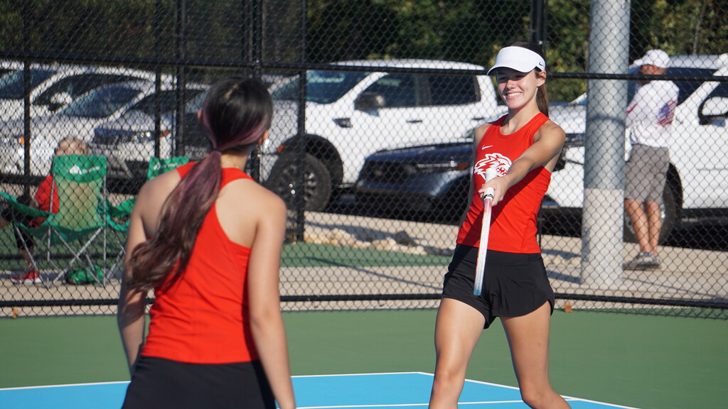 Issie smiles and holds out racket.