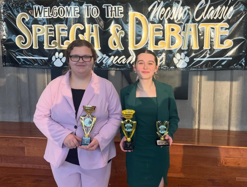 girl in pink suit holding trophy and girl in green suit holding trophy