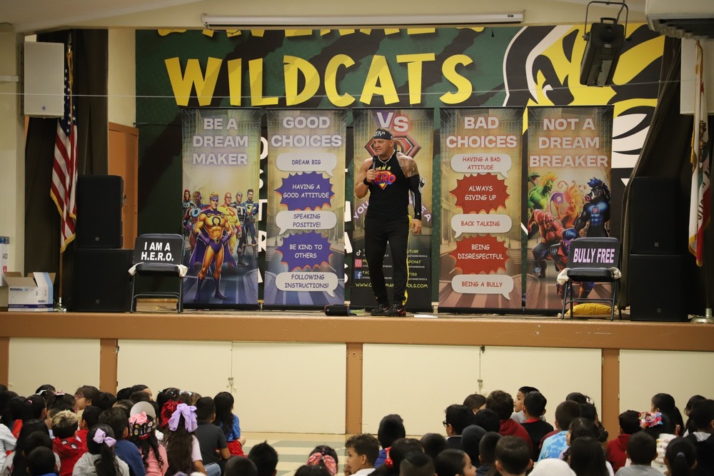 AES Assembly students and presenter on stage holding positive signs