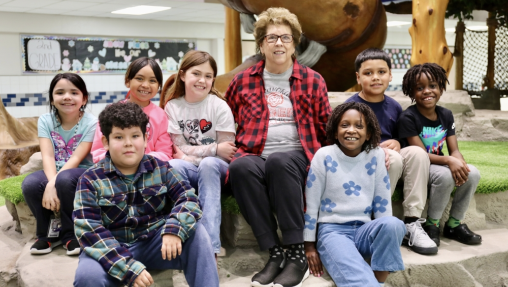 Class labeled grandma in middle of image sitting with her group of students in the center of the campus display