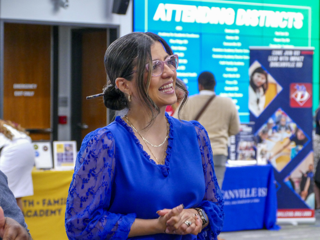 Person smiling at a school event with promotional banners for Athens District visible in the background.