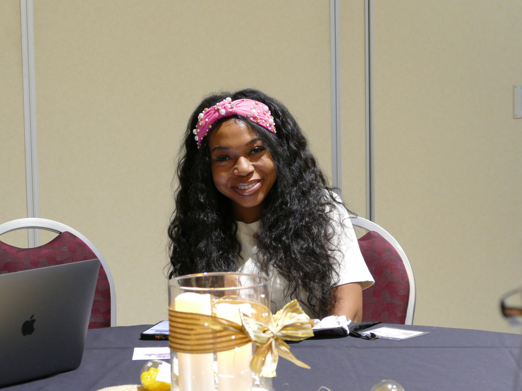 Person smiling at a conference table with a laptop displaying the Apple logo, in a well-lit room.