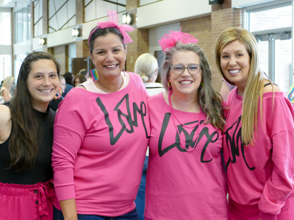 Four ladies dressing up with colorful pink shirts at a conference and smiling at the camera.