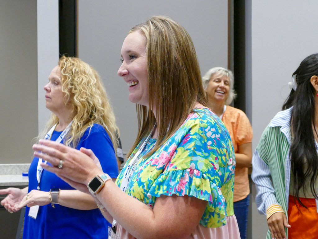 A lady smiling and clapping at an activity in a room full of people smiling and laughing.