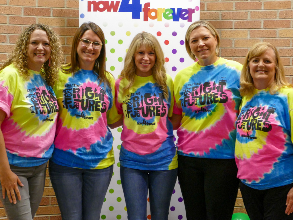 Five ladies wearing tie die shirts, smiling and posing a the camera