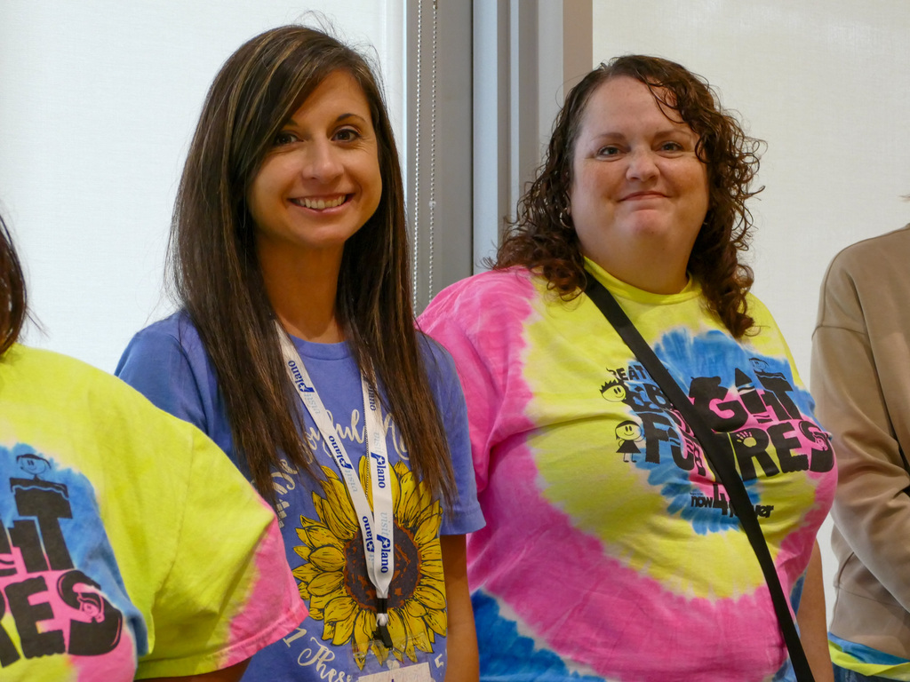 Two ladies wearing tie die shirts smiling at the camera while at a conference
