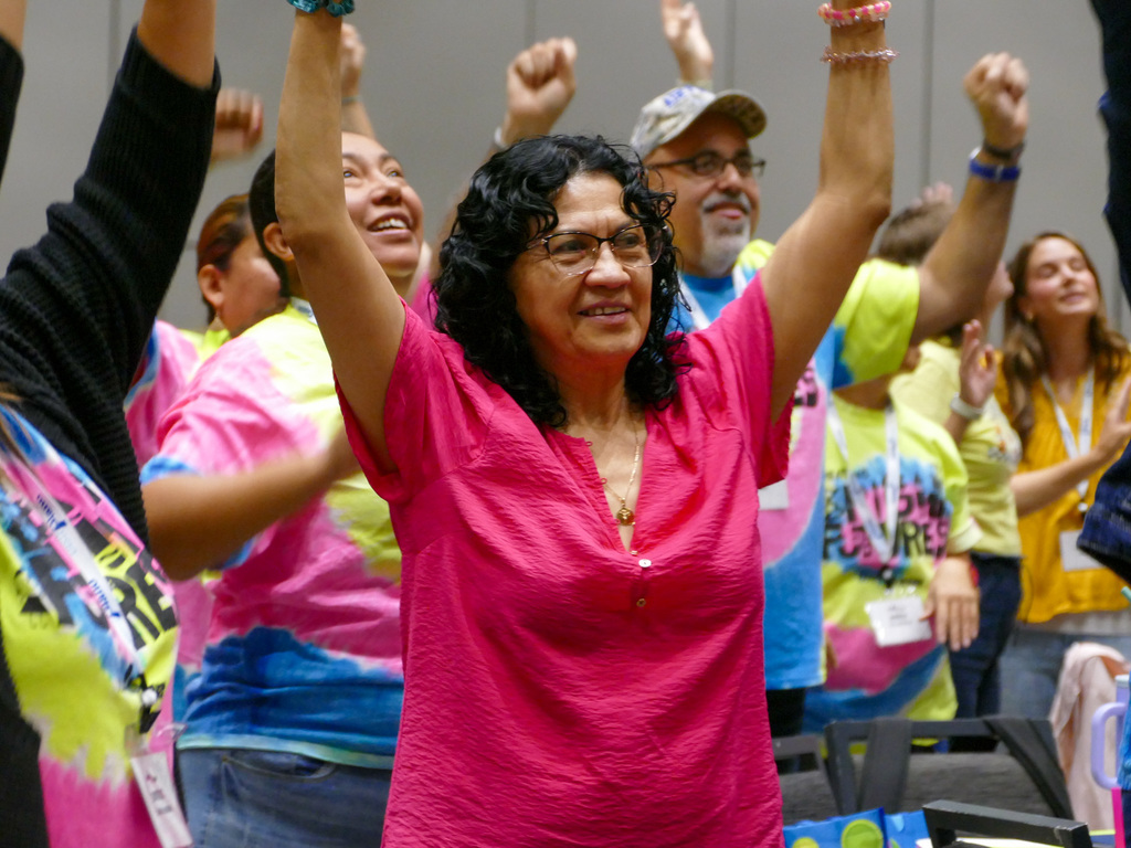 Lady wearing a bright pink shirt lifting her hands up while listening to the speaker