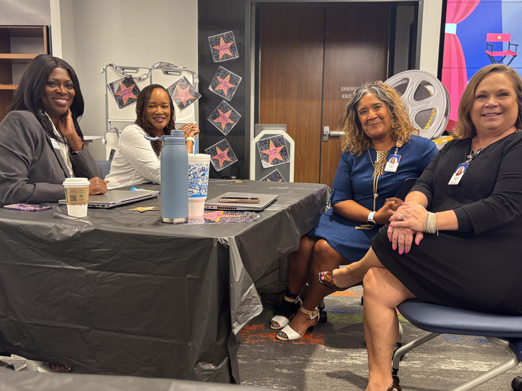 Four individuals seated at a conference table decorated with star-shaped designs, participating in a discussion in an office setting.