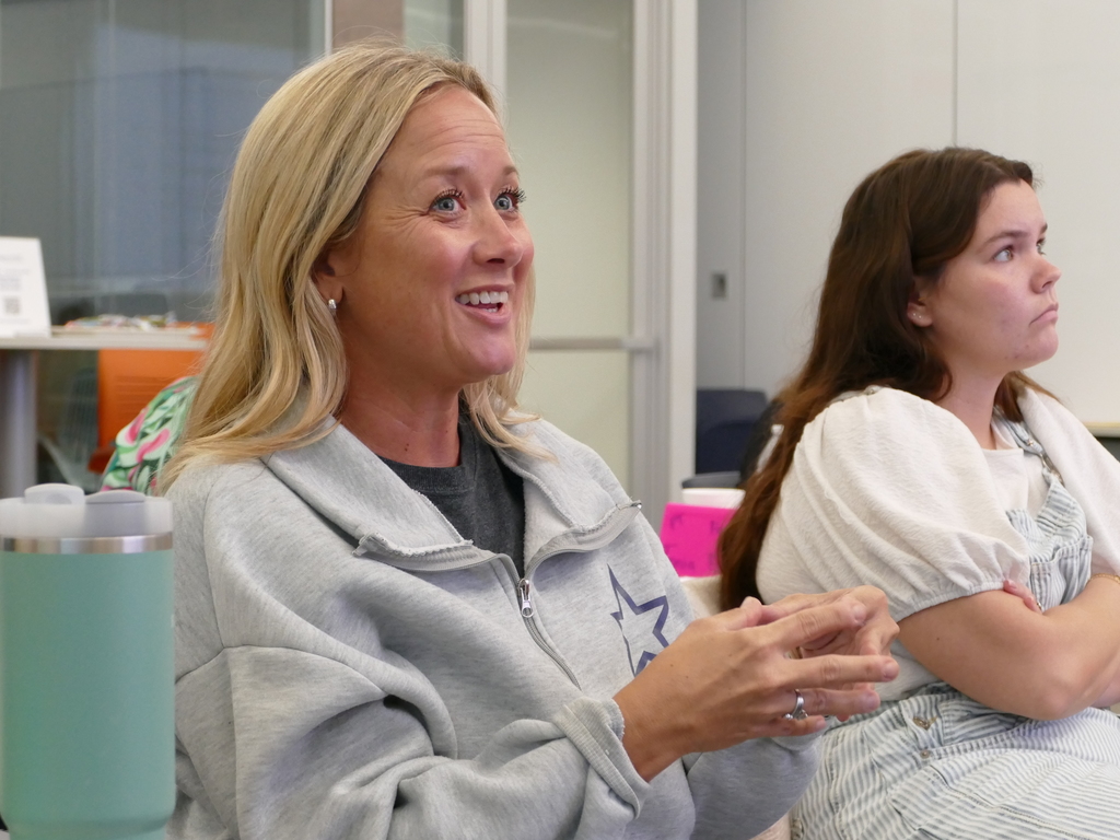 Person smiling and talking in an office environment, wearing a grey hoodie with a star logo.