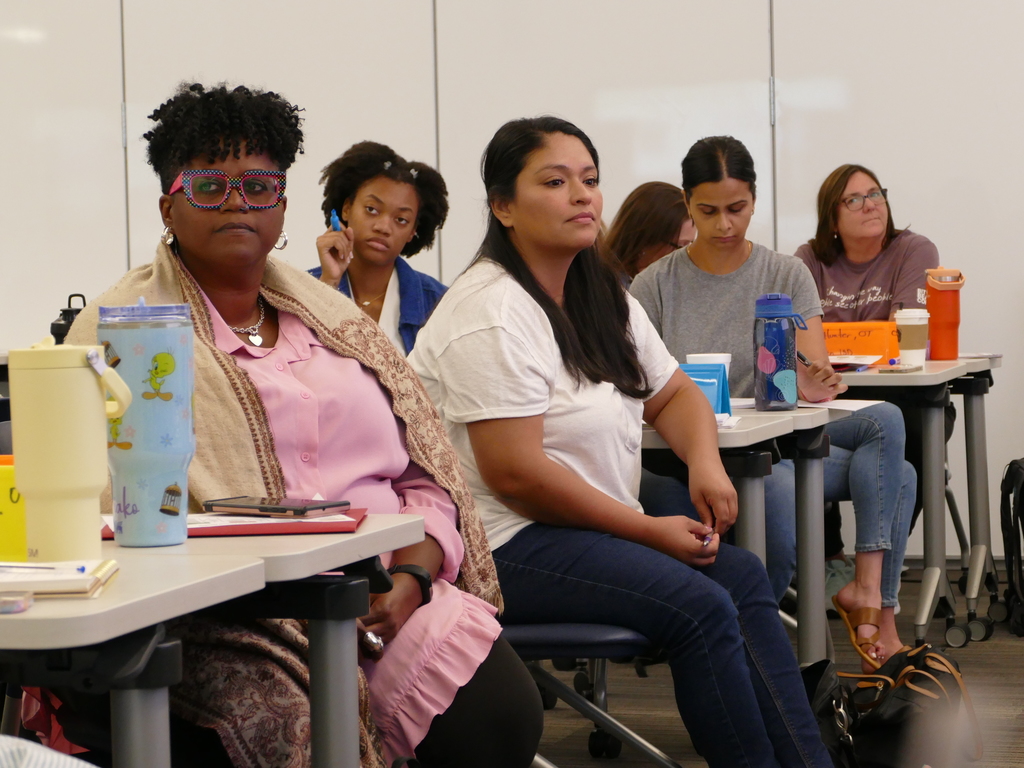 Group of attendees sitting in a classroom setting, listening attentively. Some participants are taking notes.