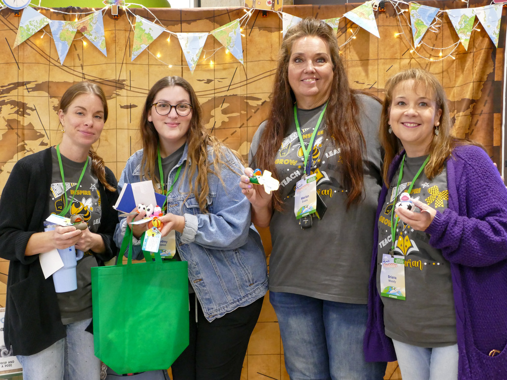 Four individuals holding plush toys at a convention, wearing event badges and matching shirts with the text "BronyCon." A rustic backdrop with festive banners hangs behind them.