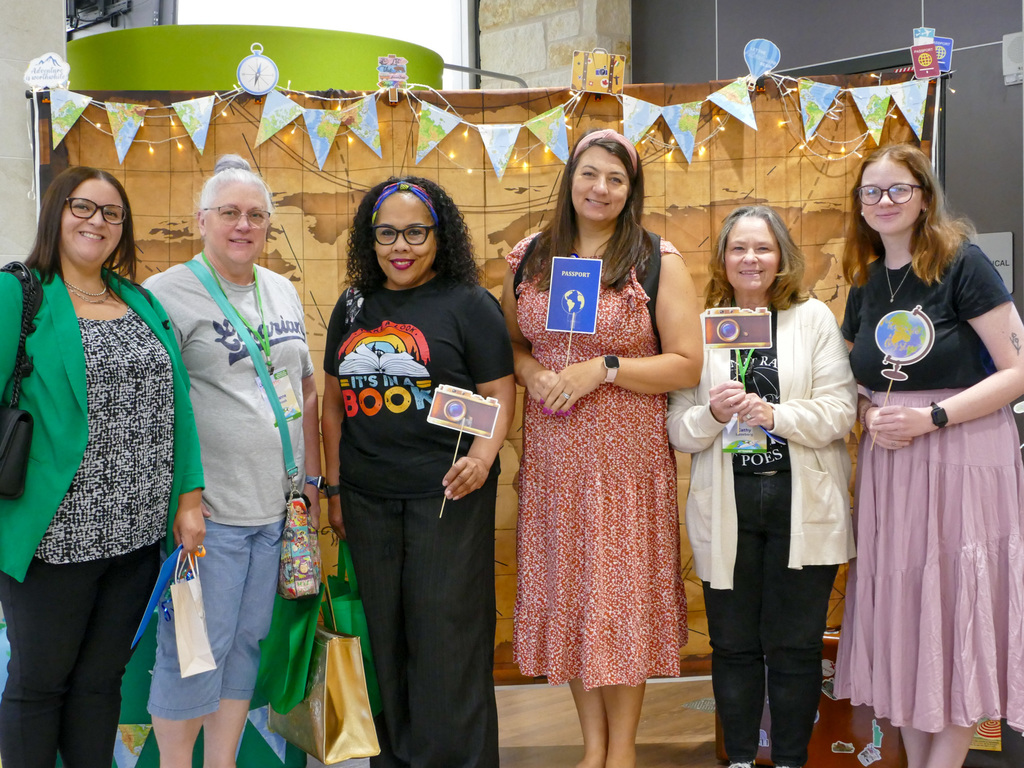 Group of six individuals standing in front of a decorated backdrop with festive banners at a book-related event, each holding a book or promotional material.