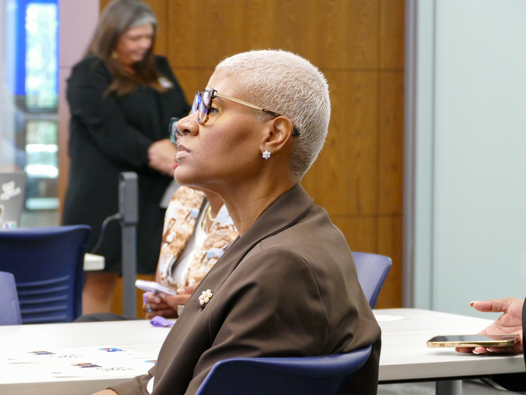 An attendee with short blonde hair and glasses, listening intently at a conference table.