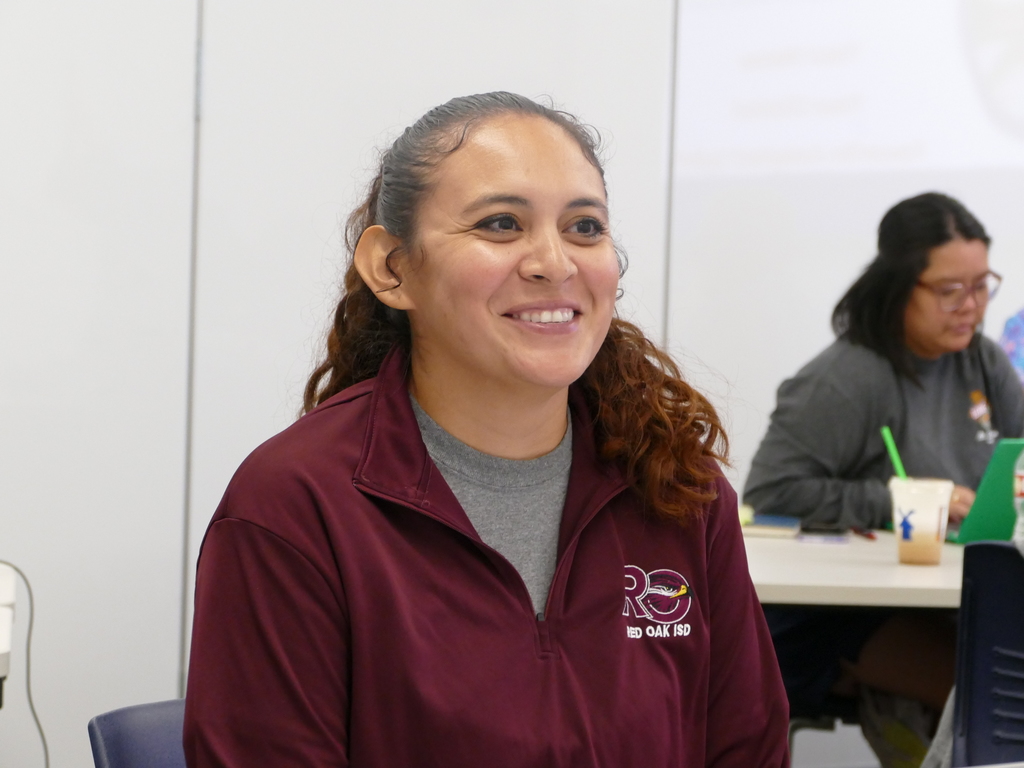 Individual smiling during a meeting, wearing a maroon Red Oak ISD jacket.