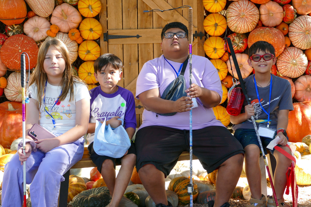 Four children sit in front of a backdrop of pumpkins and gourds, each holding a cane.
