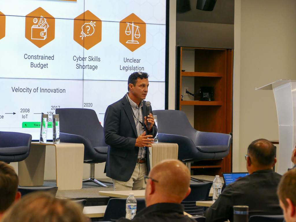 A person speaking in public, holding a mic, behind him there's a slide presentation