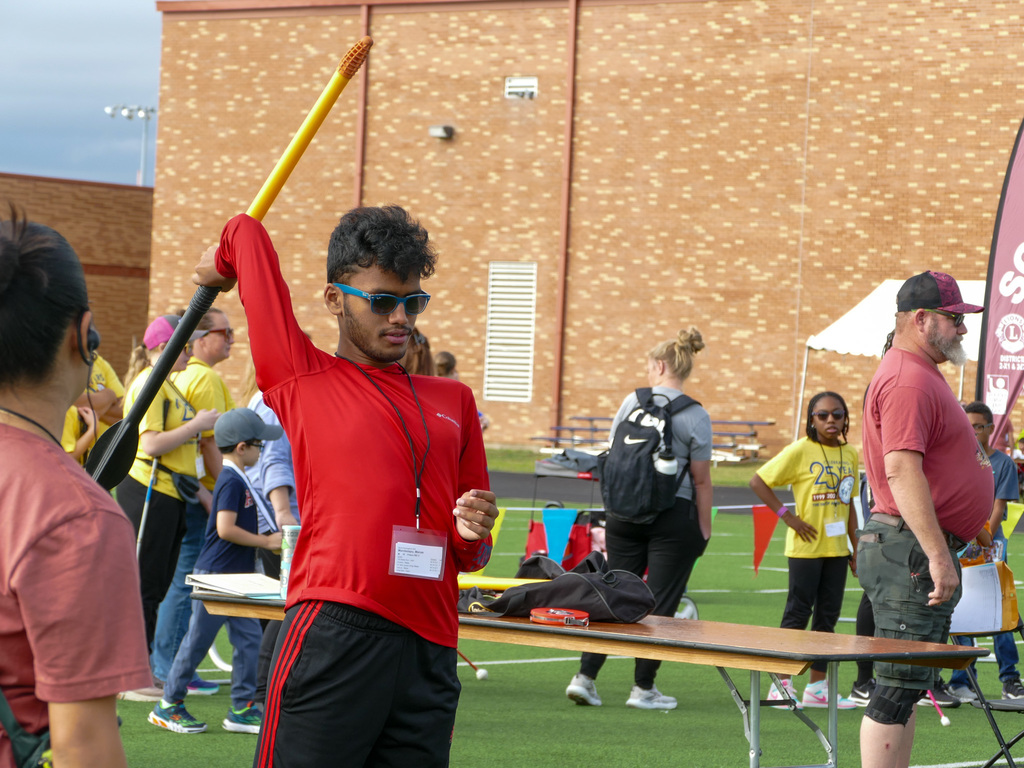 Participant at a Special Olympics event preparing to throw a javelin, surrounded by other athletes and spectators.