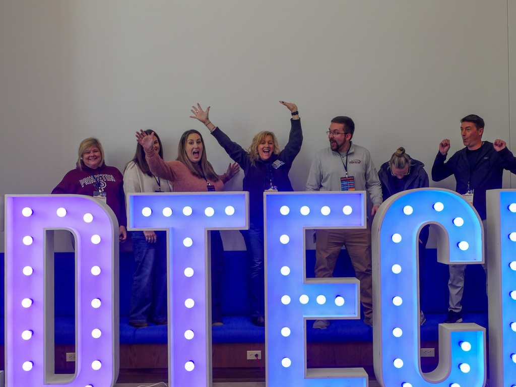 Group of people excuted smiling to the camera, behind big light up letters