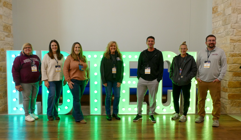 A group of people standing in front of a big light up letter sign.