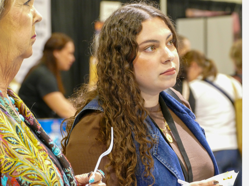 Two individuals are engaged in a conversation at a public event. One person is focused on something off-camera, displaying a thoughtful expression.