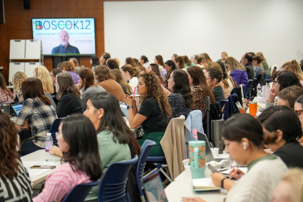 Audience at BOSC K12 conference, watching a speaker on a screen.