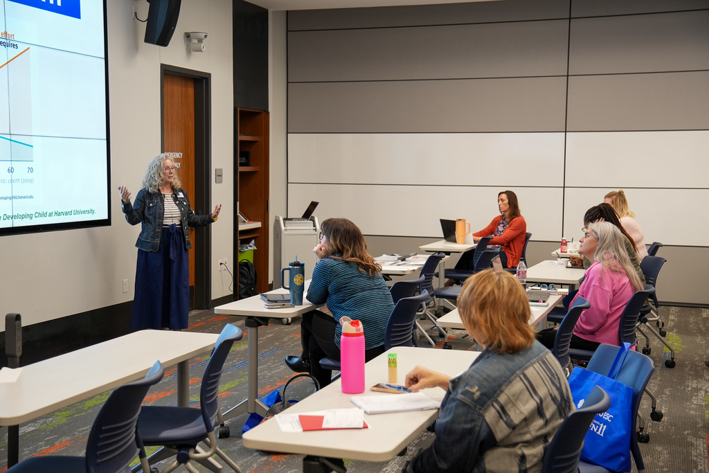 A person presenting a PowerPoint slide about data and research from Harvard to a group of attentive adults in a modern classroom.
