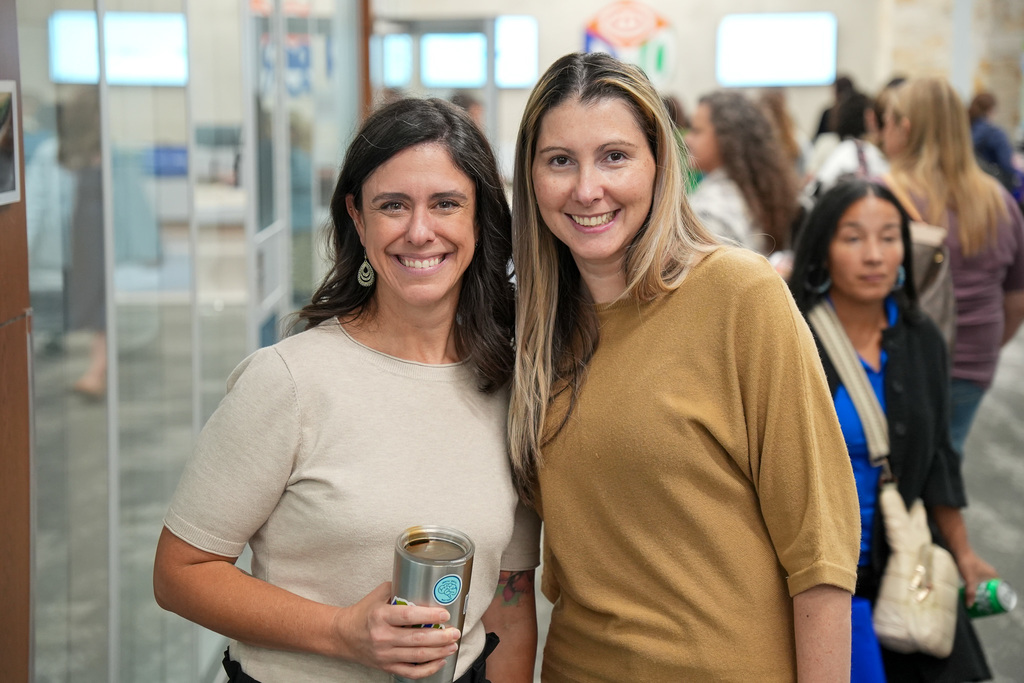 Two individuals smiling at the camera at an indoor event, holding beverages.