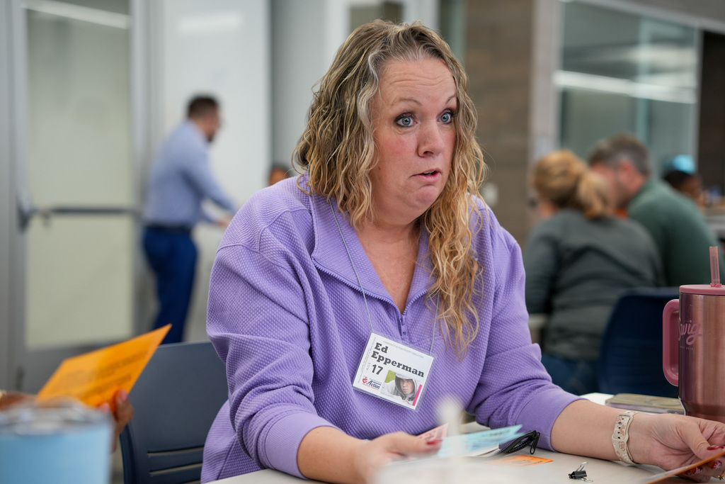 Participant with a surprised expression wearing a purple shirt and a name tag, sitting at a table during an event.