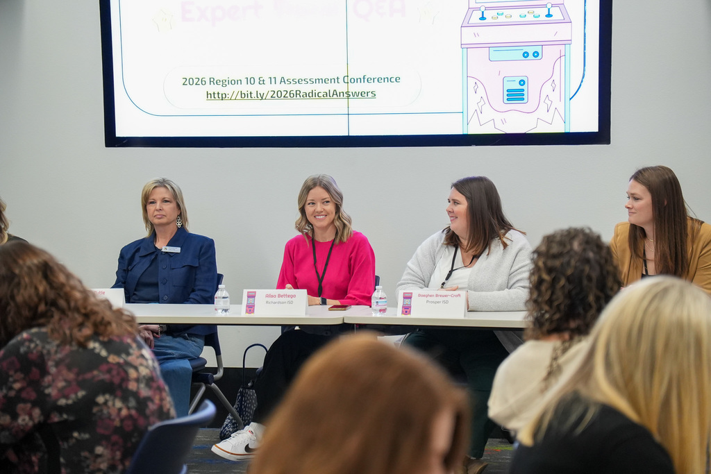 Four panelists seated at a conference table smiling and engaging with an audience during the 2026 Region 10-11 Assessment Conference. A projector screen in the background displays the conference title and a URL.