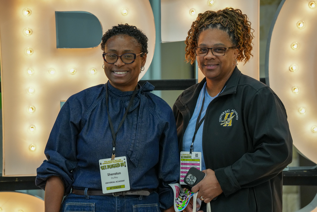 Four panelists seated at a conference table smiling and engaging with an audience during the 2026 Region 10-11 Assessment Conference. A projector screen in the background displays the conference title and a URL.