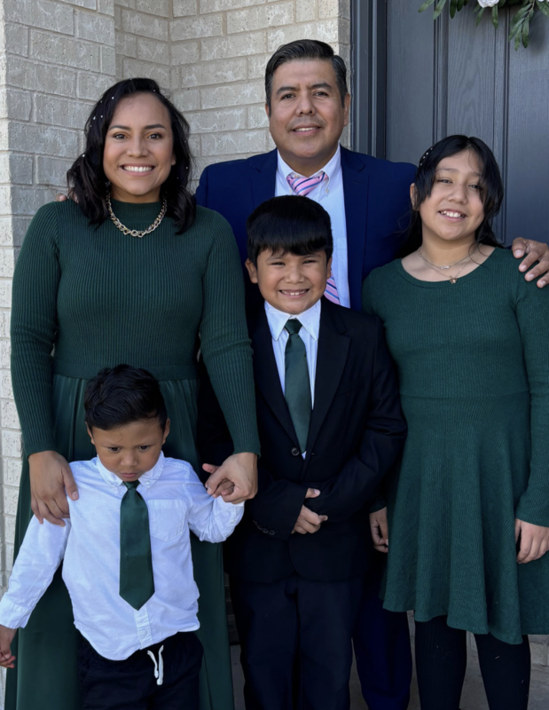 Family from the article standing in front of a black painted door to a home, in their matching green holiday outfits