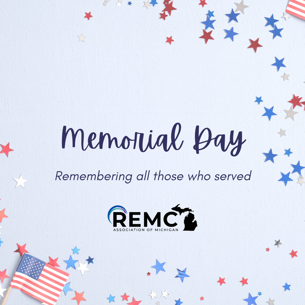  Graphic with the words “Memorial Day” in large script text and “Remembering all those who served” underneath. The design features red, white and blue star confetti around the border and a small American flag in the bottom left corner on a light background.