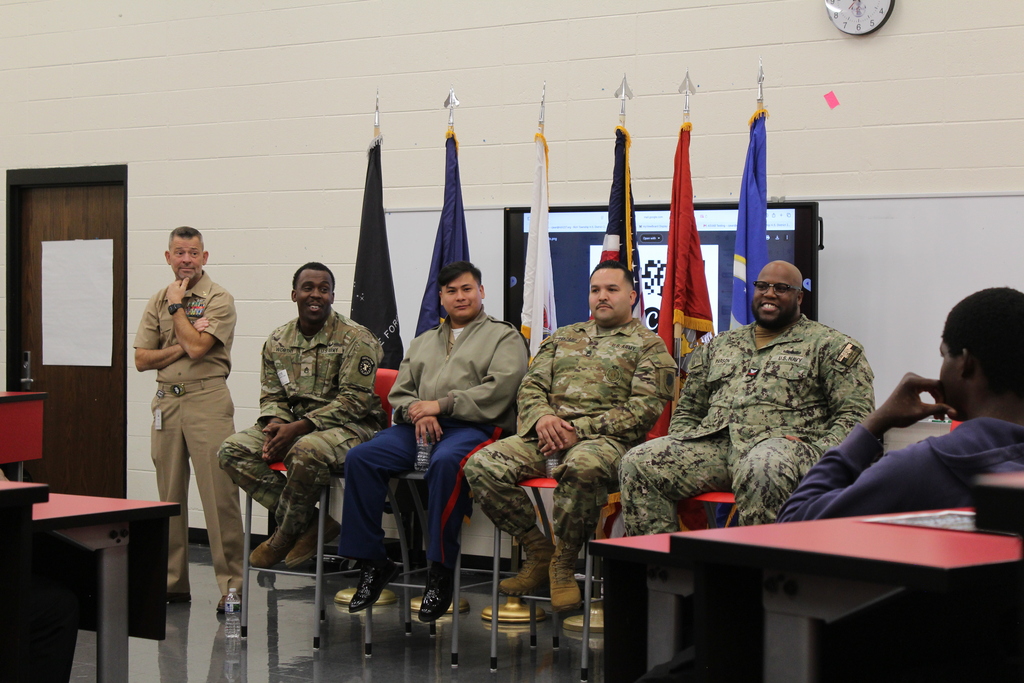 English: Graphic in Rich Township red, black, and white featuring military panelists seated beneath service flags. Text reads “Military Roundtable / Mesa Redonda Militar,” followed by “Students. Service. Conversation. / Estudiantes. Servicio. Diálogo.” and #RichInStudentSuccess.  Español: Gráfico en rojo, negro y blanco de Rich Township que muestra a miembros de un panel militar sentados frente a banderas. El texto dice “Military Roundtable / Mesa Redonda Militar”, seguido de “Students. Service. Conversation. / Estudiantes. Servicio. Diálogo.” y #RichInStudentSuccess.