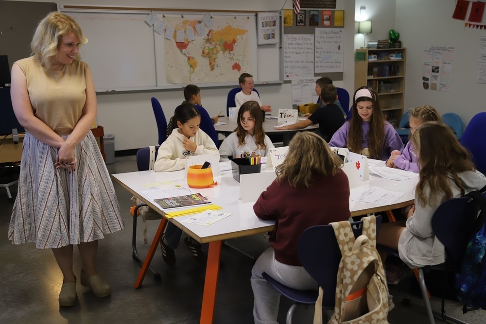 Wisdomr Ridge teacher Victoria Cox stands smiling and looking over a table of students working on a project in class