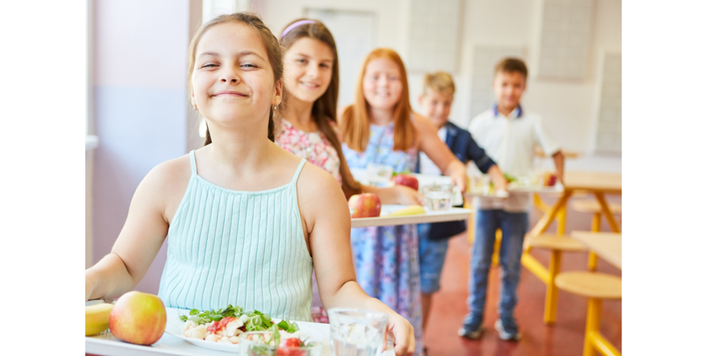 Smiling female students standing in line holding food trays during lunch time in school cafeteria