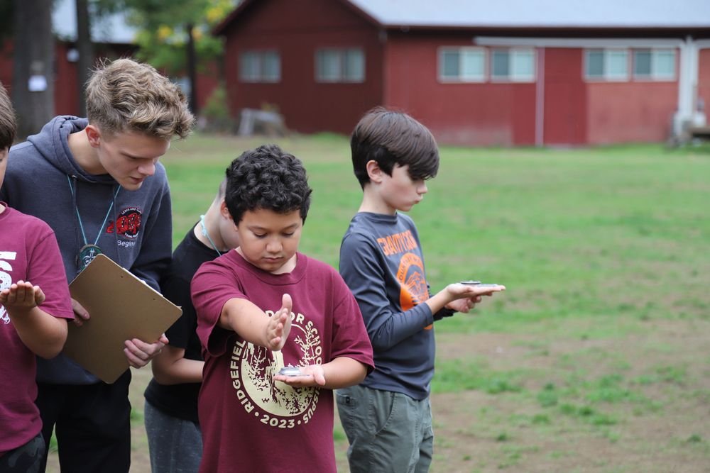 a 5th grader using a compass with help from a high school student camp counselor