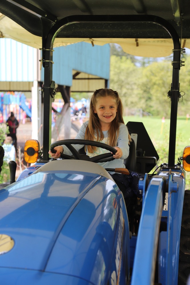 a 2nd grade students smiles as she sits behind the steering wheel of a tractor