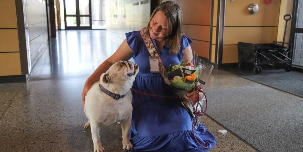 South Ridge School Counselor Anne Lamping kneeling next to an English bulldog and holding a bouquet of flowers