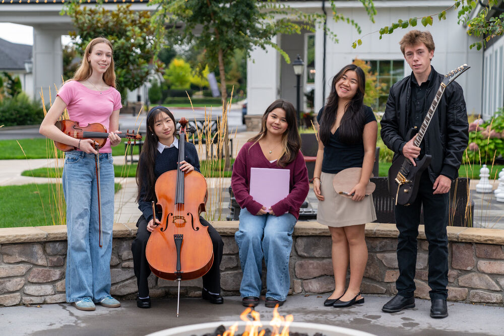 Five high school students posing with their instruments in an outdoor area with trees in the background