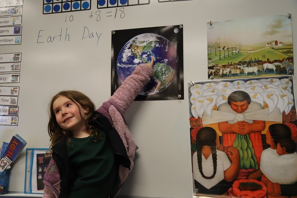 A smiling kindergarten student points to an art print of planet  Earth