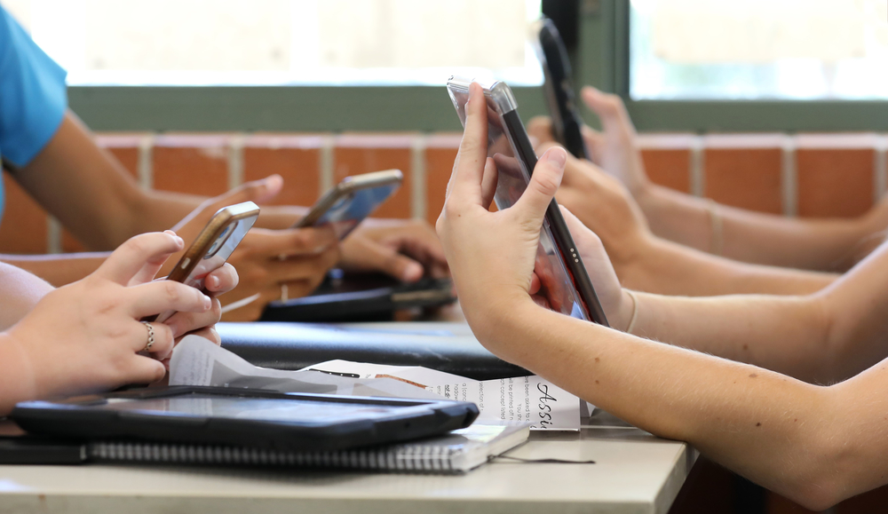 students sitting at a table holding and looking at their cell phones