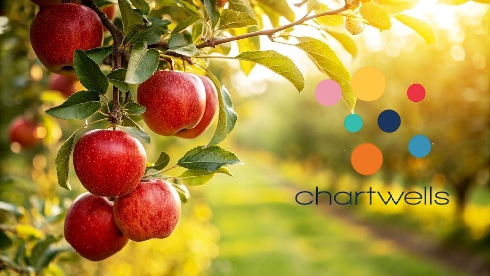 Apples hang from a tree with the sun shining through branches, and the Chartwells logo