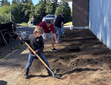 An elementary student and adult volunteers use shovels to dig out and replace old soil.