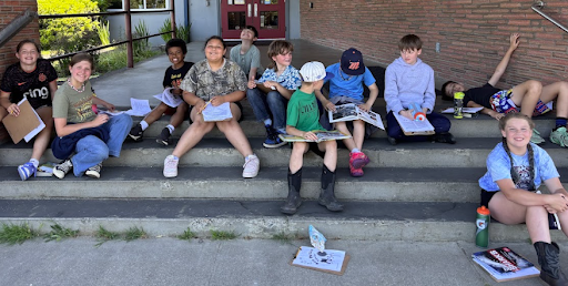 11 elementary school students sit on the steps outside of the Union Ridge main office waiting to plant native plants