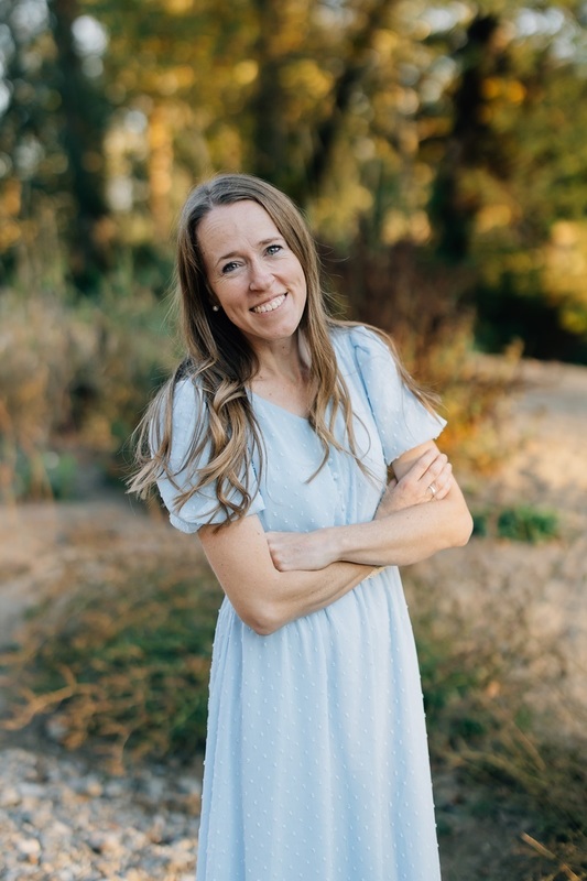 Charlotte Barnes smiling and wearing a light blue dress standing in front of trees 