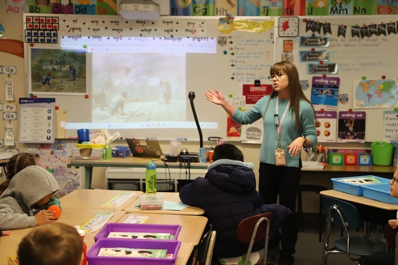 Teacher Shandel Oderman standing at the front of her classroom gesturing towards artwork hung on the whiteboard