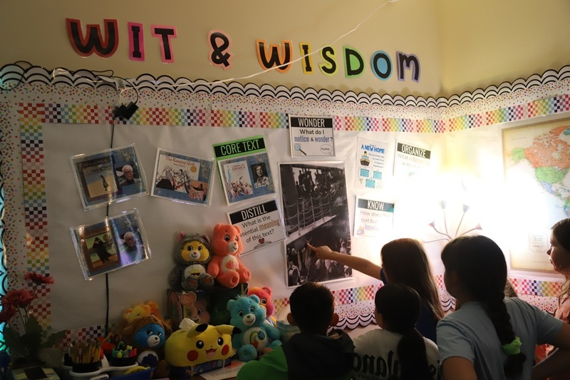 Elementary school students standing around an art print depicting immigrants  on a large ship